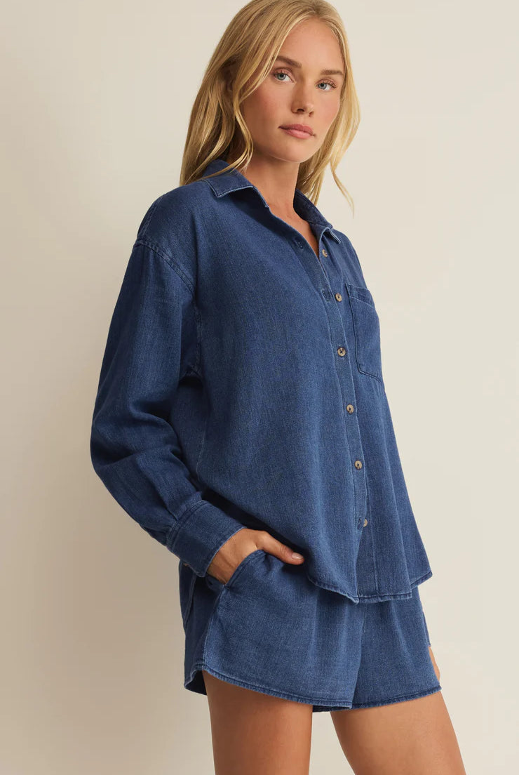 Woman wearing a blue denim shirt and shorts set against a beige background