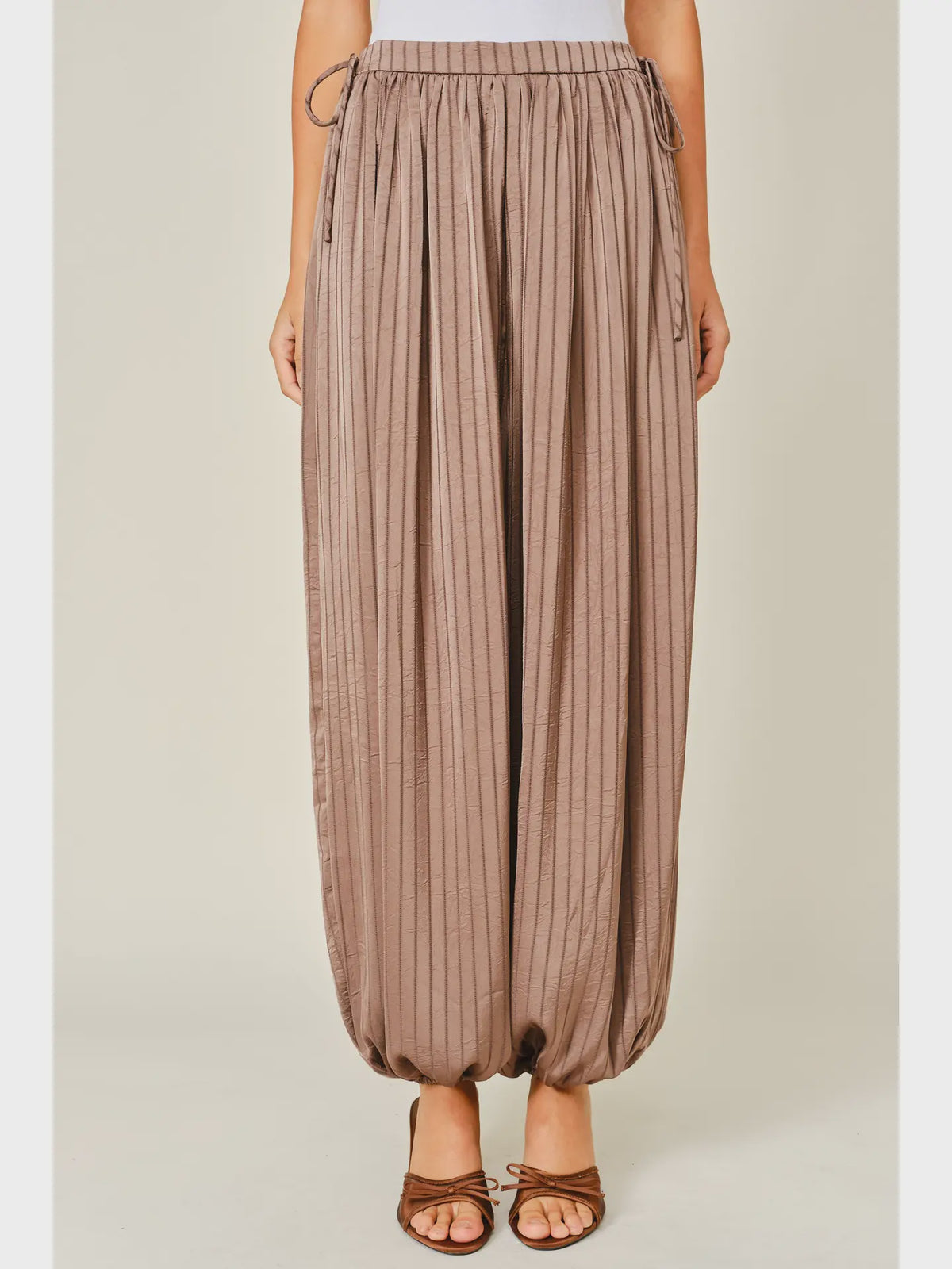Zola Striped Satin Bubble Pants featuring a soft, glossy satin finish with a striped pattern, comfortable elastic waistband, adjustable drawstring side details, and functional side pockets. Designed with a relaxed, voluminous balloon silhouette and a flowy, lightweight feel for an effortlessly chic look.