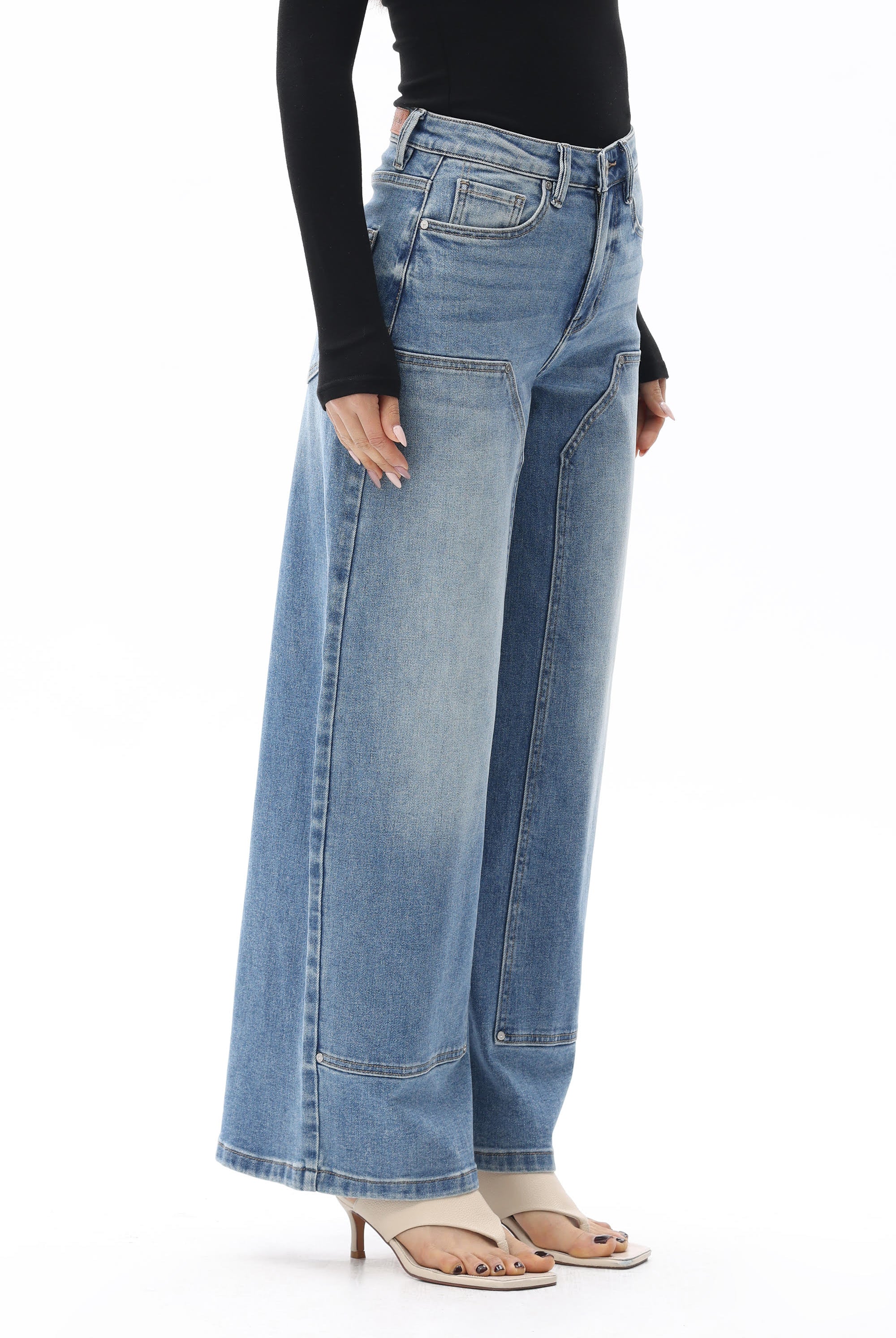 Model wearing BAYEAS Valentine High Rise Barrel Jeans in a medium blue wash, featuring a high-rise waist, relaxed barrel-leg silhouette, subtle fading, front panel seam detailing, classic five-pocket styling, and a full-length fit. Styled with a black long-sleeve top and nude thong sandals.
