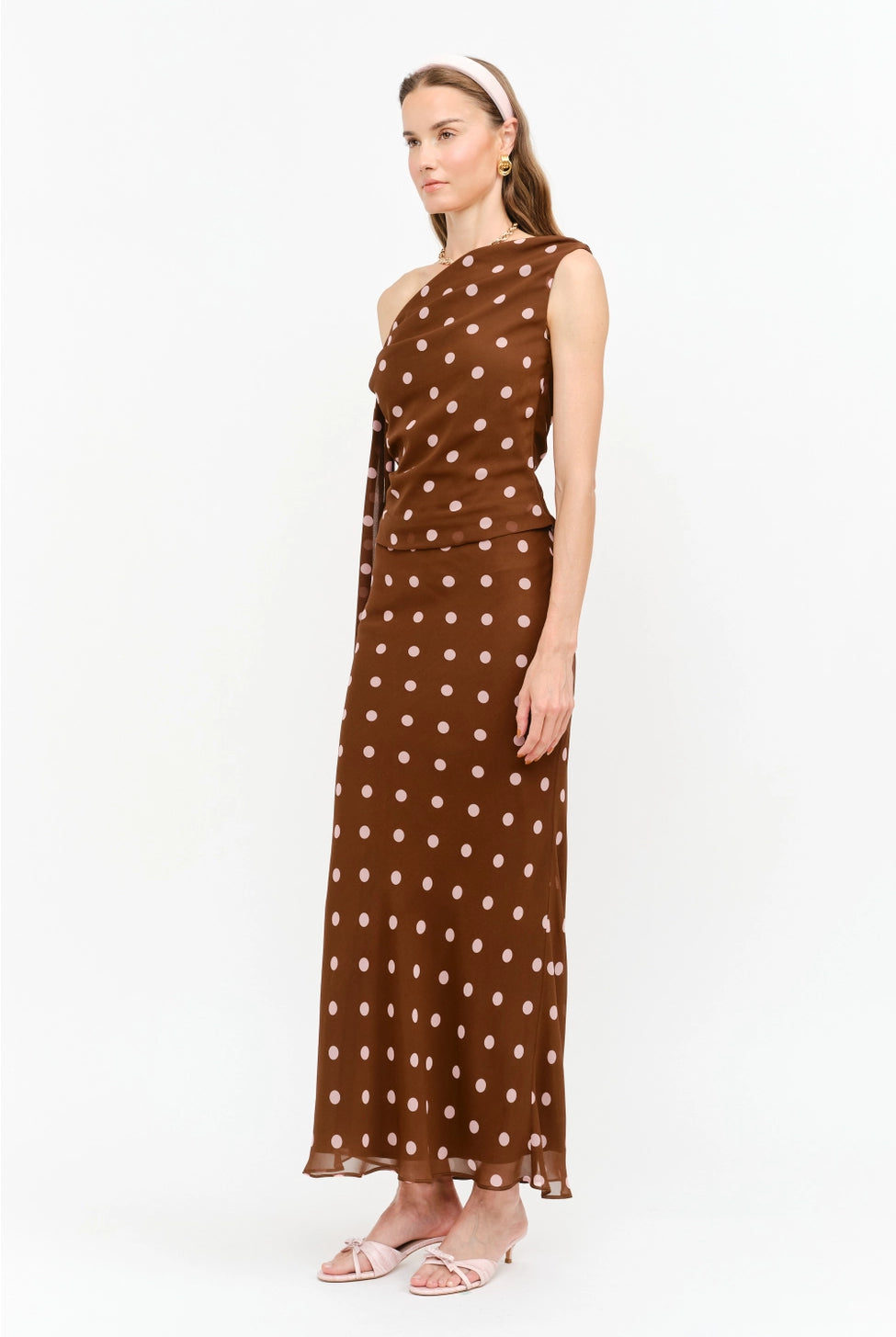 Celestine Off the Shoulder Top in brown featuring soft pink polka dots, an asymmetrical one-shoulder neckline, and a draped tie detail along the arm.