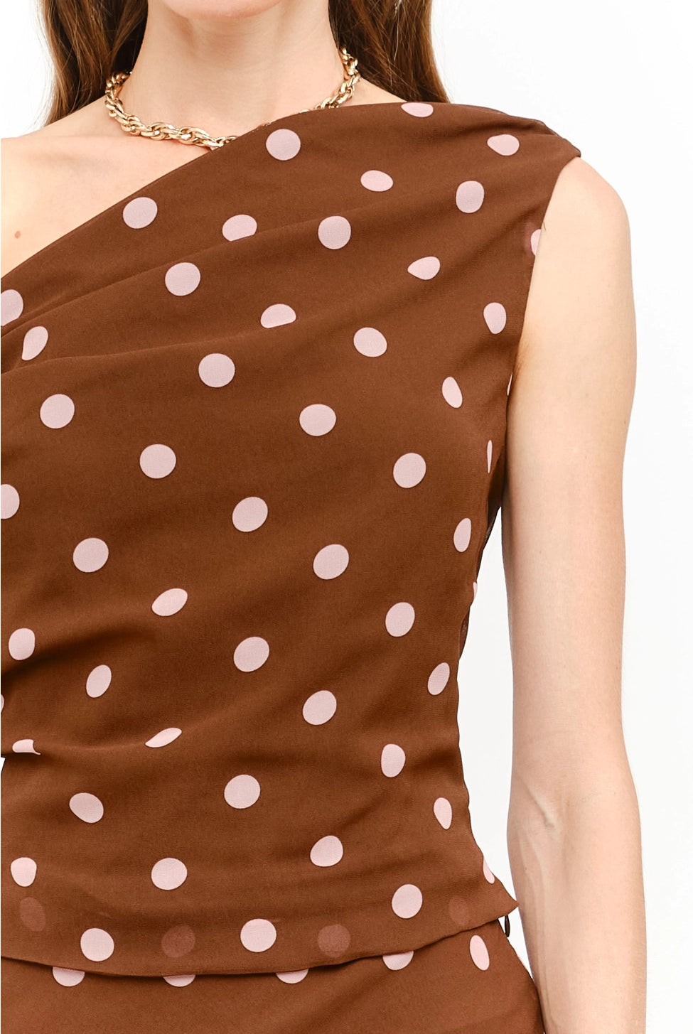 Celestine Off the Shoulder Top in brown featuring soft pink polka dots, an asymmetrical one-shoulder neckline, and a draped tie detail along the arm.