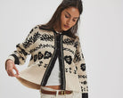 Woman wearing a patterned cardigan over a white shirt and beige shorts on a white background