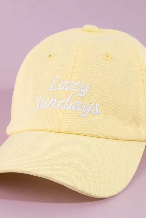 A pale yellow cotton baseball cap with 'Lazy Sundays' embroidered in white script on the front