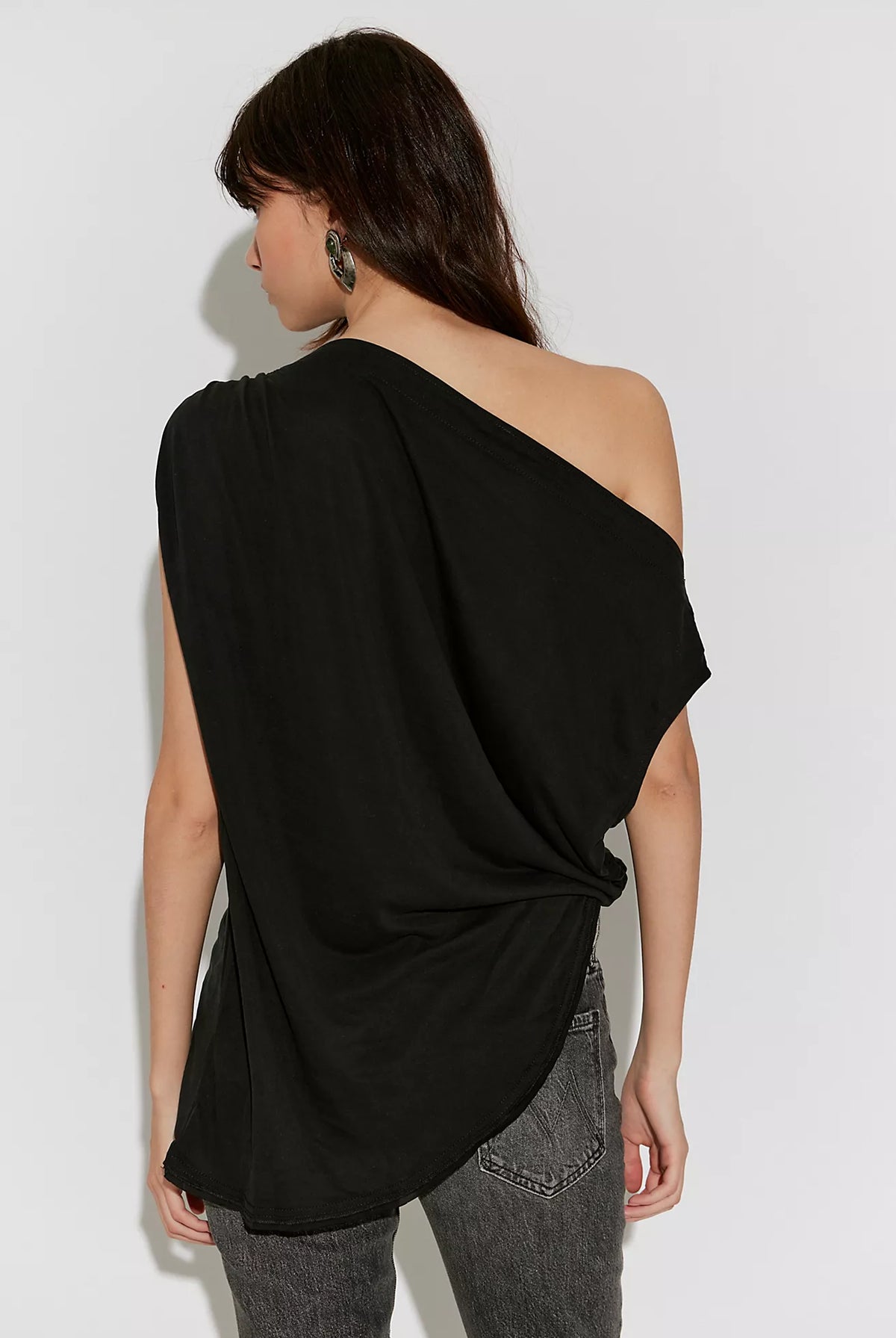 Cascadia Tunic in black featuring a draped off-the-shoulder neckline, soft slinky jersey fabric, ruched detailing, long sleeves, a relaxed longline silhouette, and an asymmetrical hem.