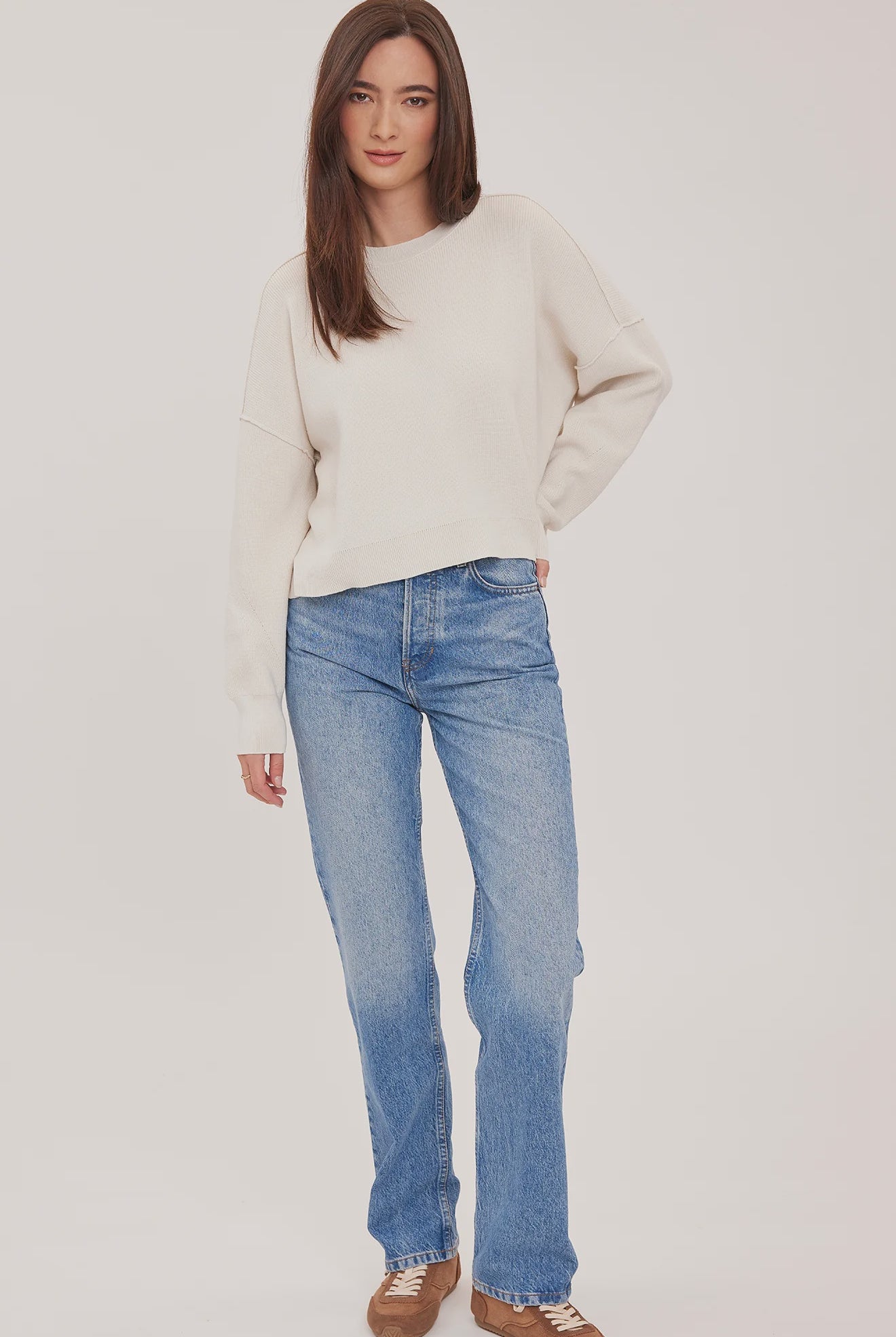 Women's cream oversized knit pullover sweater featuring a classic crew neckline, exposed seam detailing, side slits, and a soft textured half-cardigan stitch.