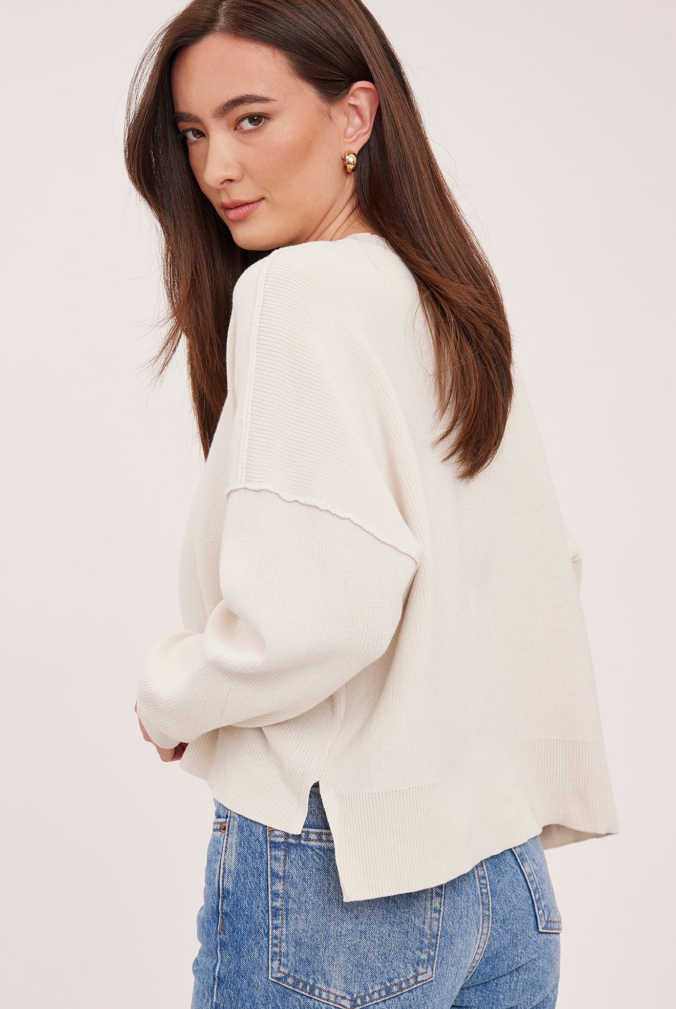Women's cream oversized knit pullover sweater featuring a classic crew neckline, exposed seam detailing, side slits, and a soft textured half-cardigan stitch.