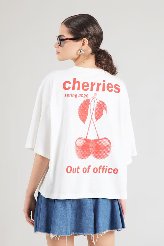 Person wearing a white t-shirt with red cherry design and text on a plain background