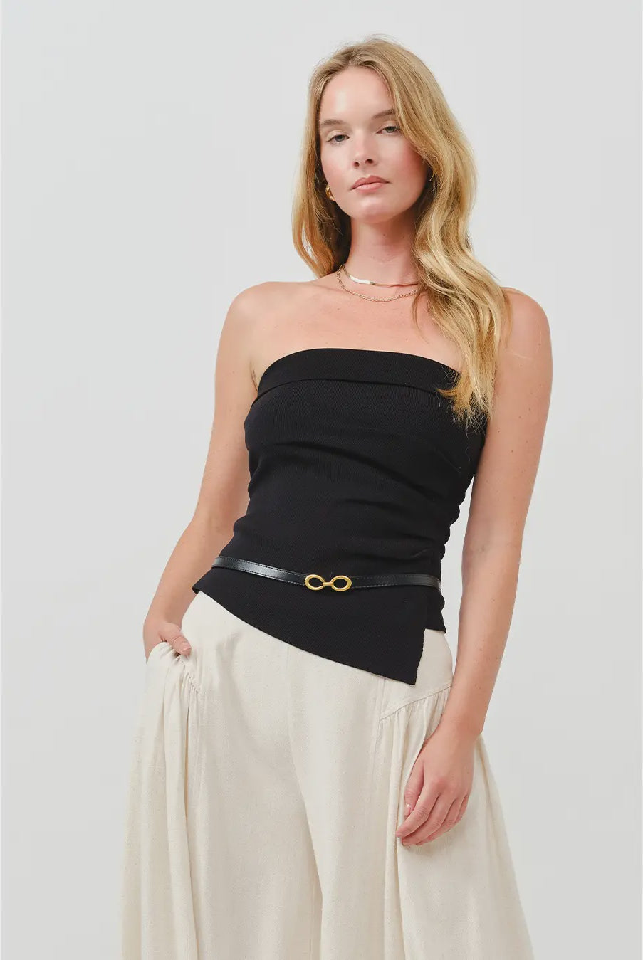 Woman wearing a black strapless top with a belt and beige pants on a white background