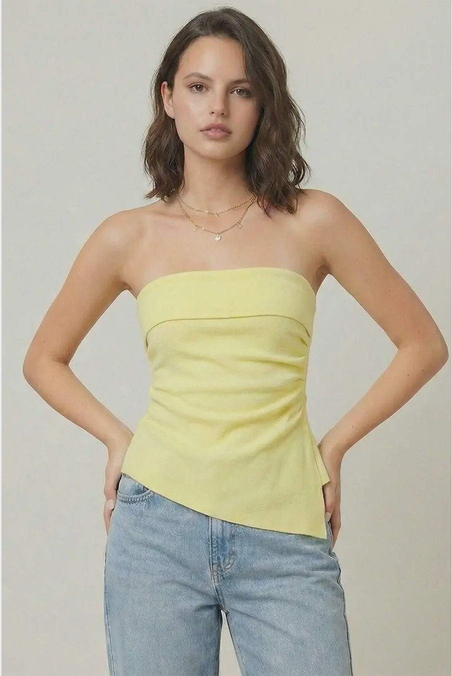 Woman wearing a strapless yellow top and blue jeans against a plain background
