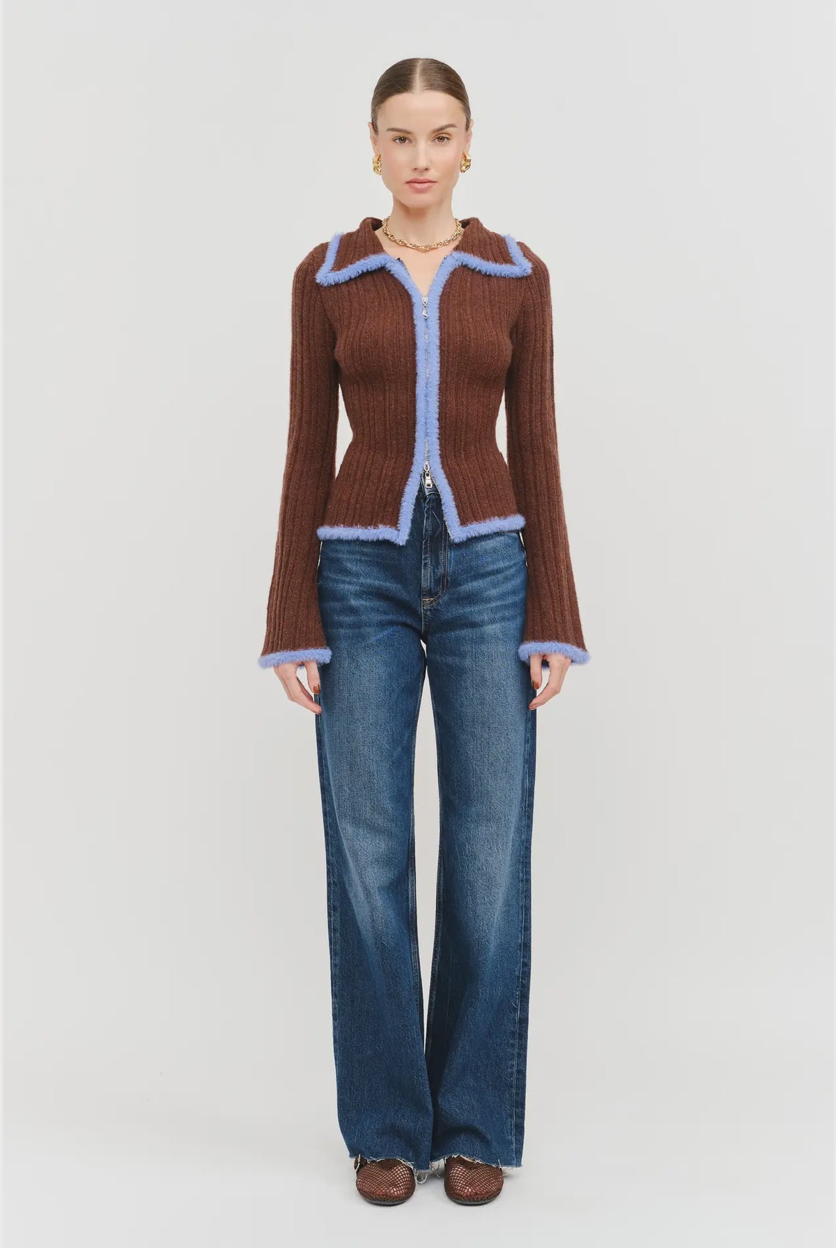 Model wearing the Jacquie Knit Top in brown, featuring a fitted silhouette, long sleeves, collared neckline, contrasting blue fuzzy trim, and two-way front zipper closure.