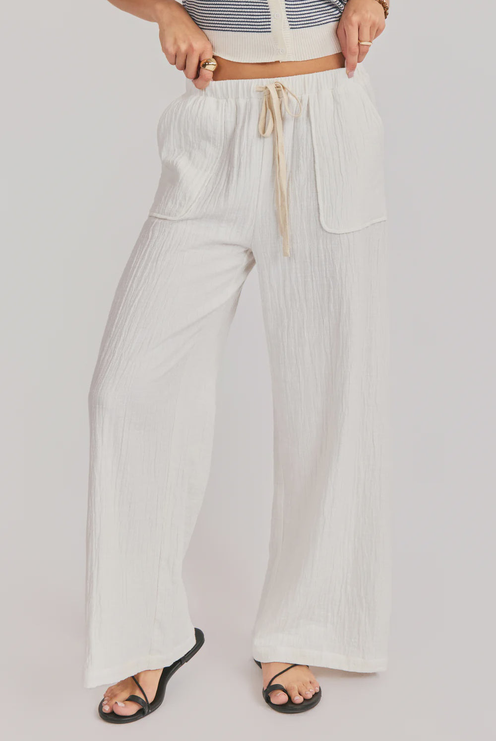 Person wearing light-colored wide-leg pants with a drawstring on a plain background