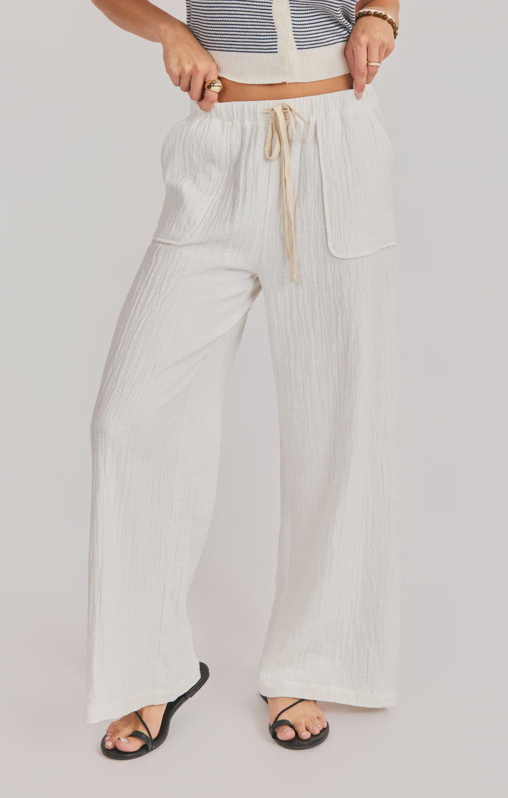 Person wearing light-colored wide-leg pants with a drawstring on a plain background