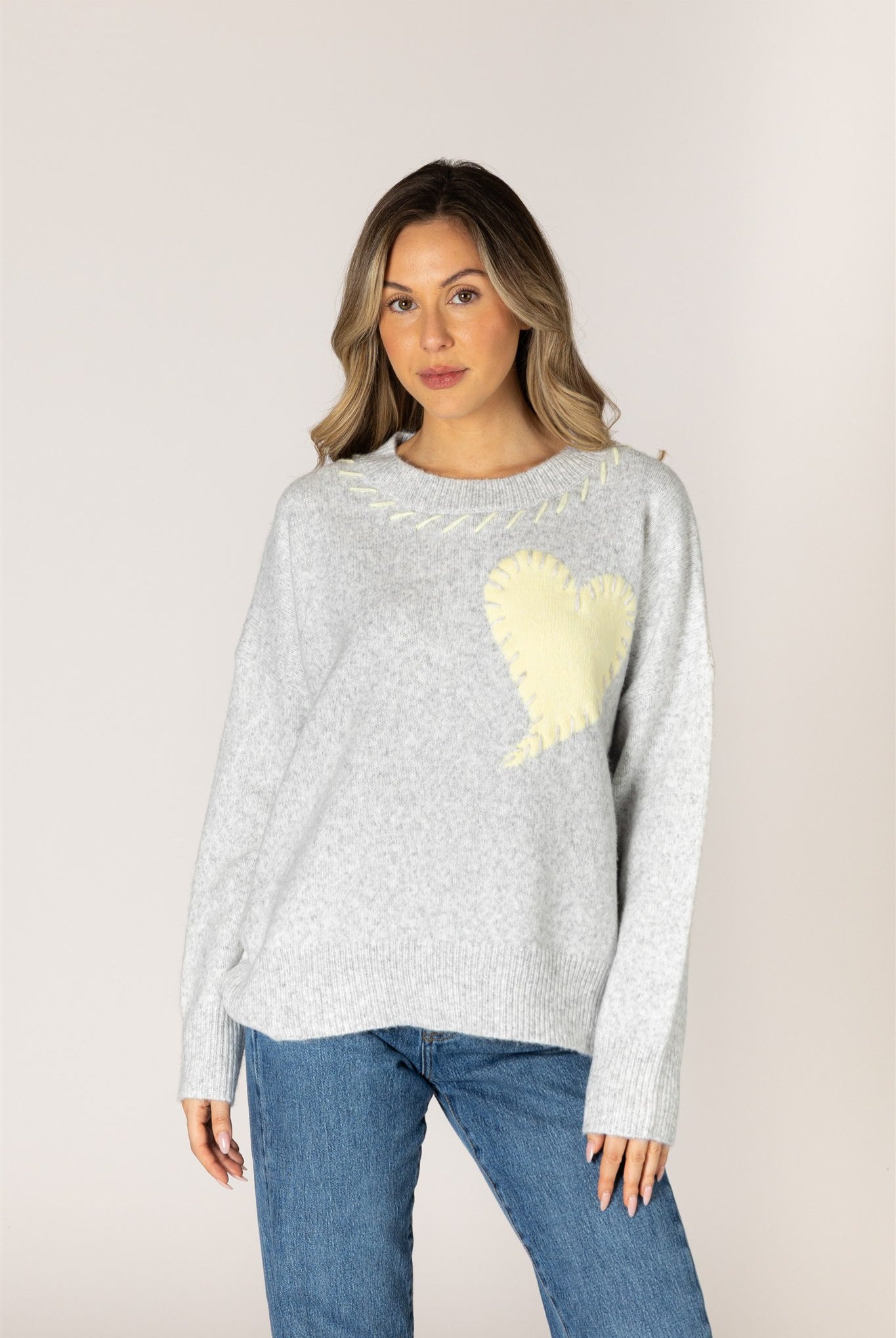 Ash grey crewneck sweater featuring a pale lemonade heart appliqué with contrast whipstitch detailing, long sleeves, and ribbed cuffs, hem, and neckline.