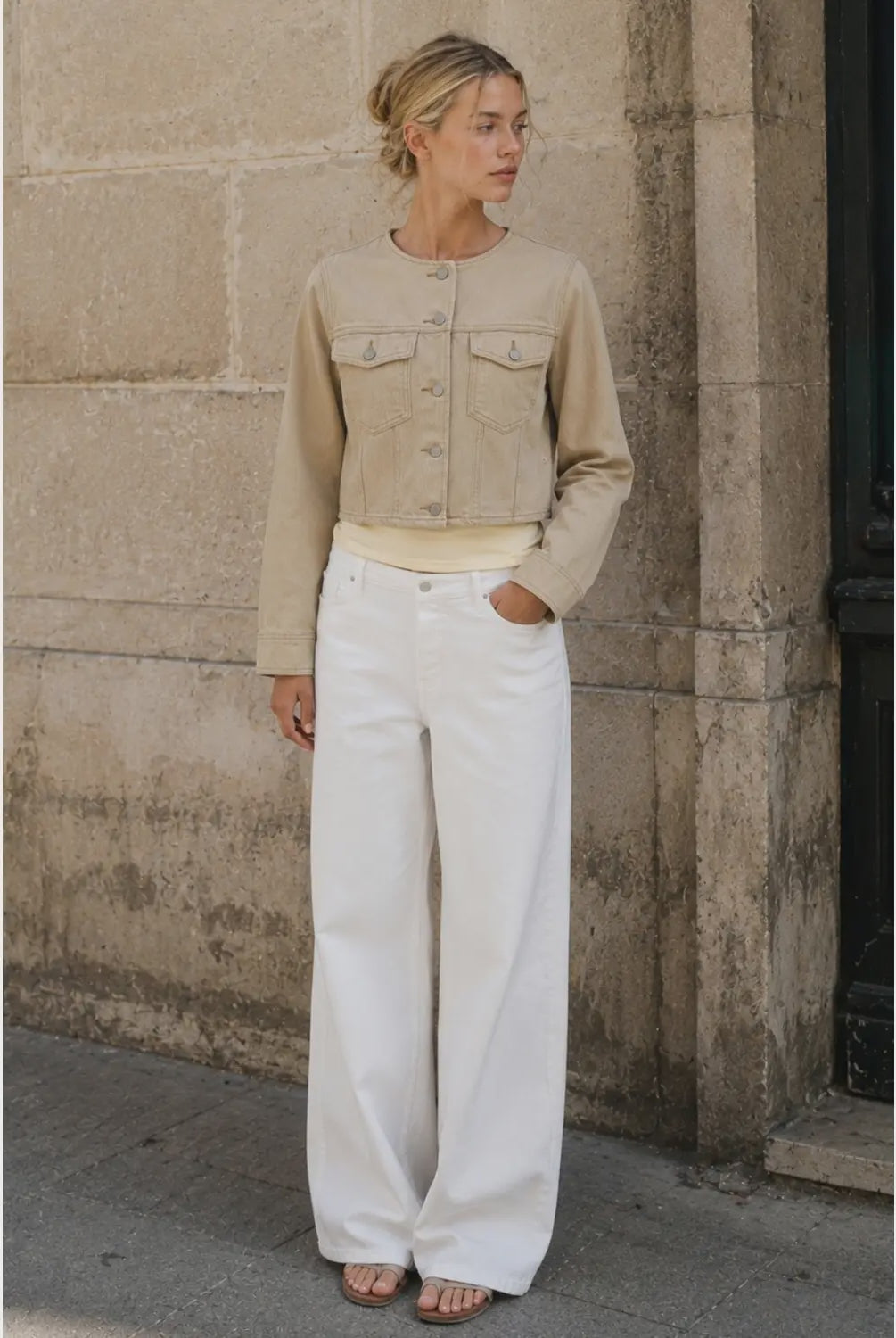 The Veda Cropped Utility Jacket in a soft sand denim wash, featuring a collarless neckline, flap chest pockets, structured seam detailing, and a cropped silhouette.