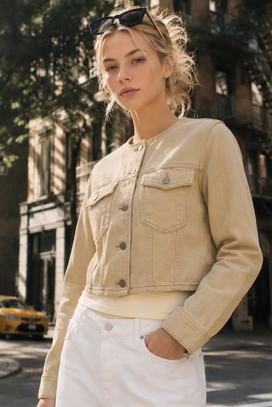 The Veda Cropped Utility Jacket in a soft sand denim wash, featuring a collarless neckline, flap chest pockets, structured seam detailing, and a cropped silhouette.