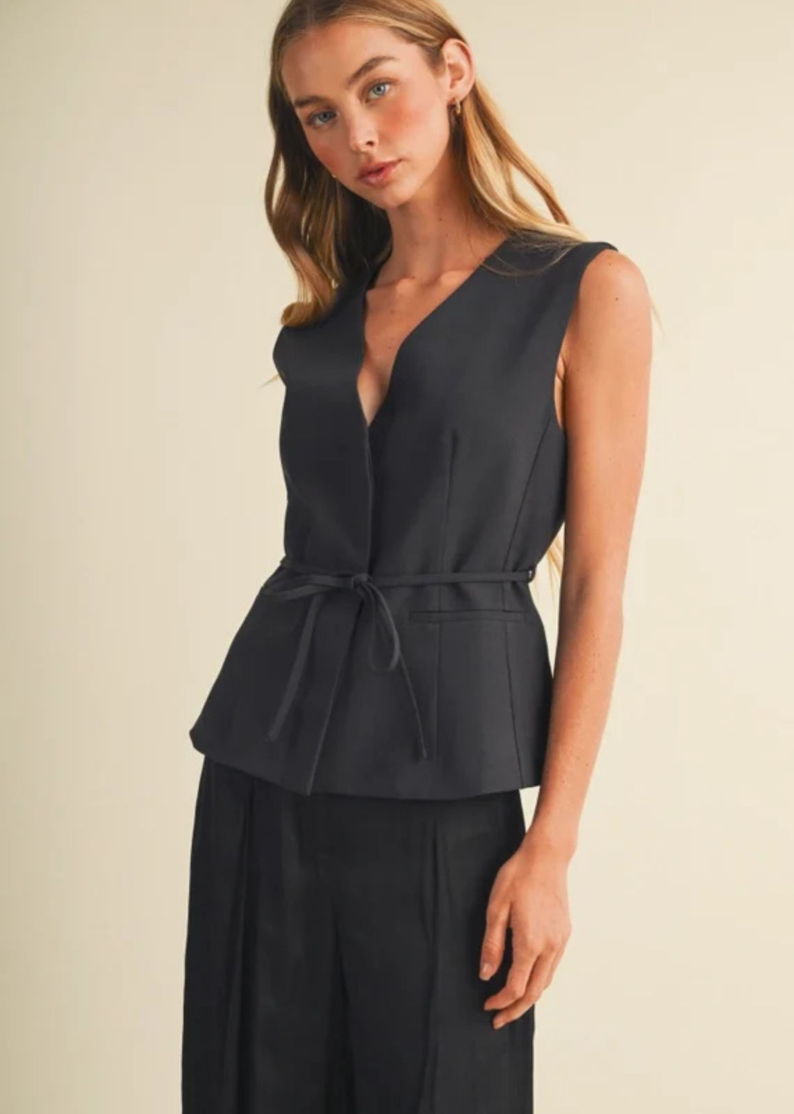 Tailored peplum top in high-density woven suiting, featuring princess seams, a deep surplice V-neckline, removable self-tie waist belt, extended shoulders, and a single-button closure.