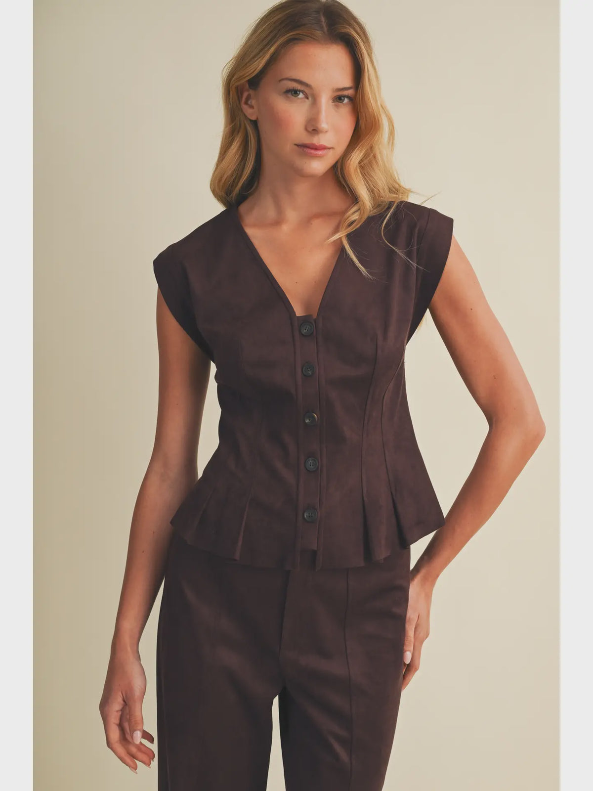 Faux suede sleeveless top with a V-neckline, button-front closure, extended shoulders, princess seams, and pleated peplum hem. Model is 5'9" and wearing a size Small.