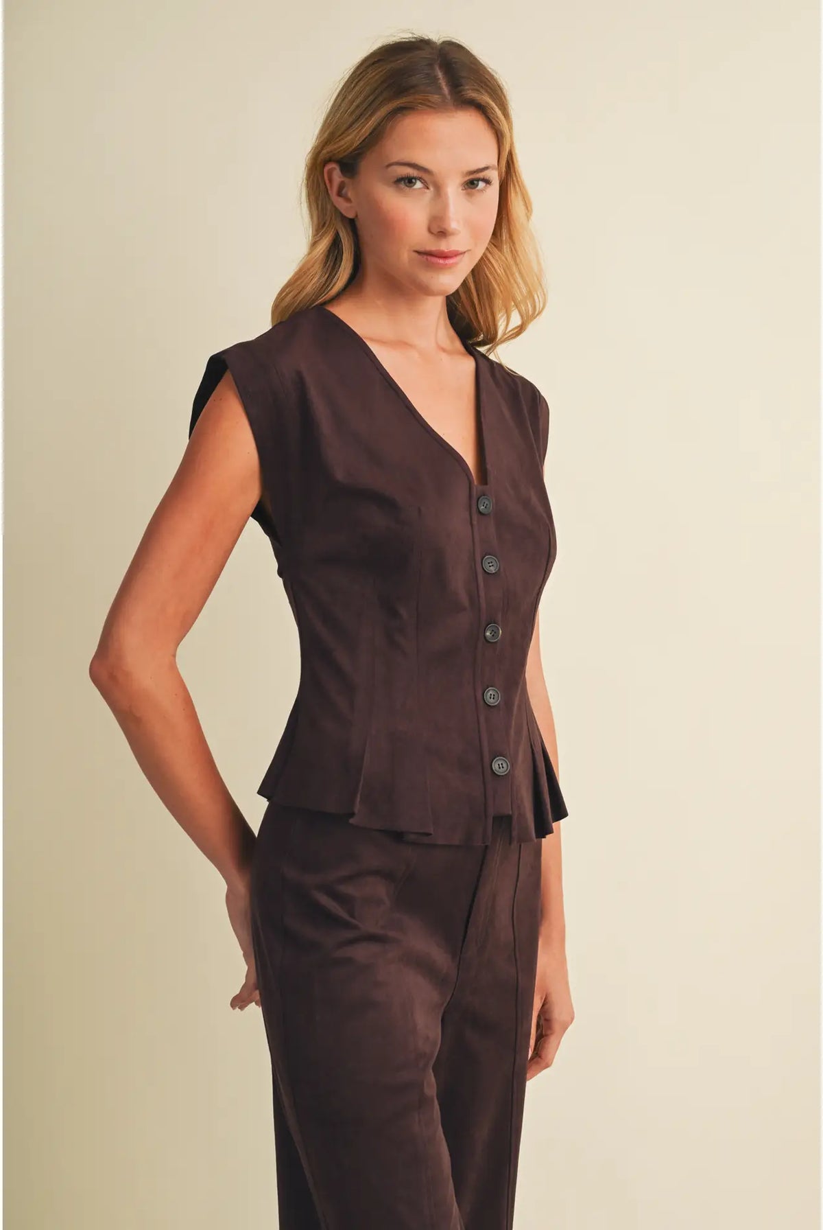 Faux suede sleeveless top with a V-neckline, button-front closure, extended shoulders, princess seams, and pleated peplum hem. Model is 5'9" and wearing a size Small.