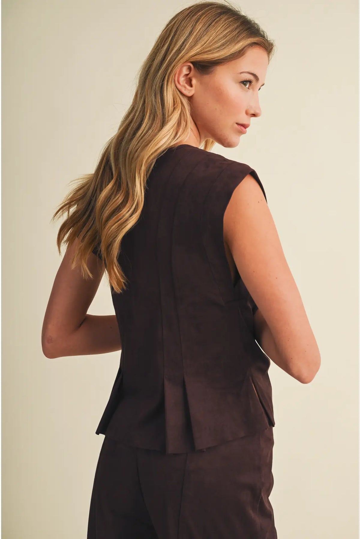 Faux suede sleeveless top with a V-neckline, button-front closure, extended shoulders, princess seams, and pleated peplum hem. Model is 5'9" and wearing a size Small.