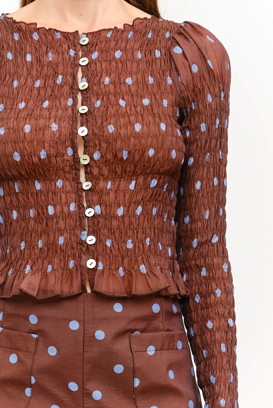 Women’s brown polka dot smocked long sleeve top featuring front buttons, puff sleeves, a fitted silhouette, and ruffled hem.