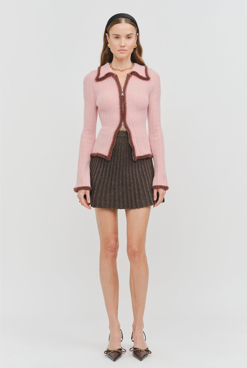 Model wearing the Jacquie Knit Top in light pink, featuring a fitted silhouette, long sleeves, collared neckline, contrasting burgundy fuzzy trim, and two-way front zipper closure.