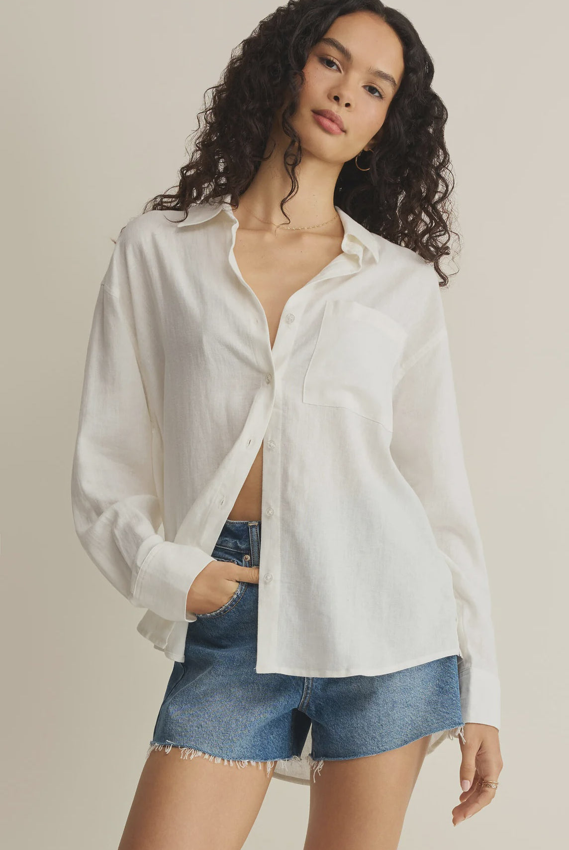 Woman wearing a white button-up shirt and denim shorts on a beige background