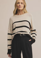 Woman wearing a cream sweater with black stripes and black pants against a beige background