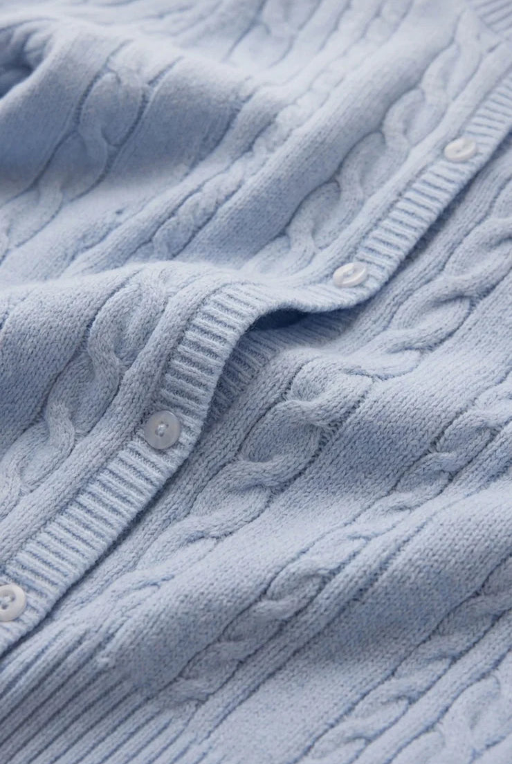 Close-up of a cable knit cardigan highlighting the textured knit pattern, crew neckline, button-front closure, and soft fabric. The detailed stitching and elevated finish showcase its classic, everyday design.