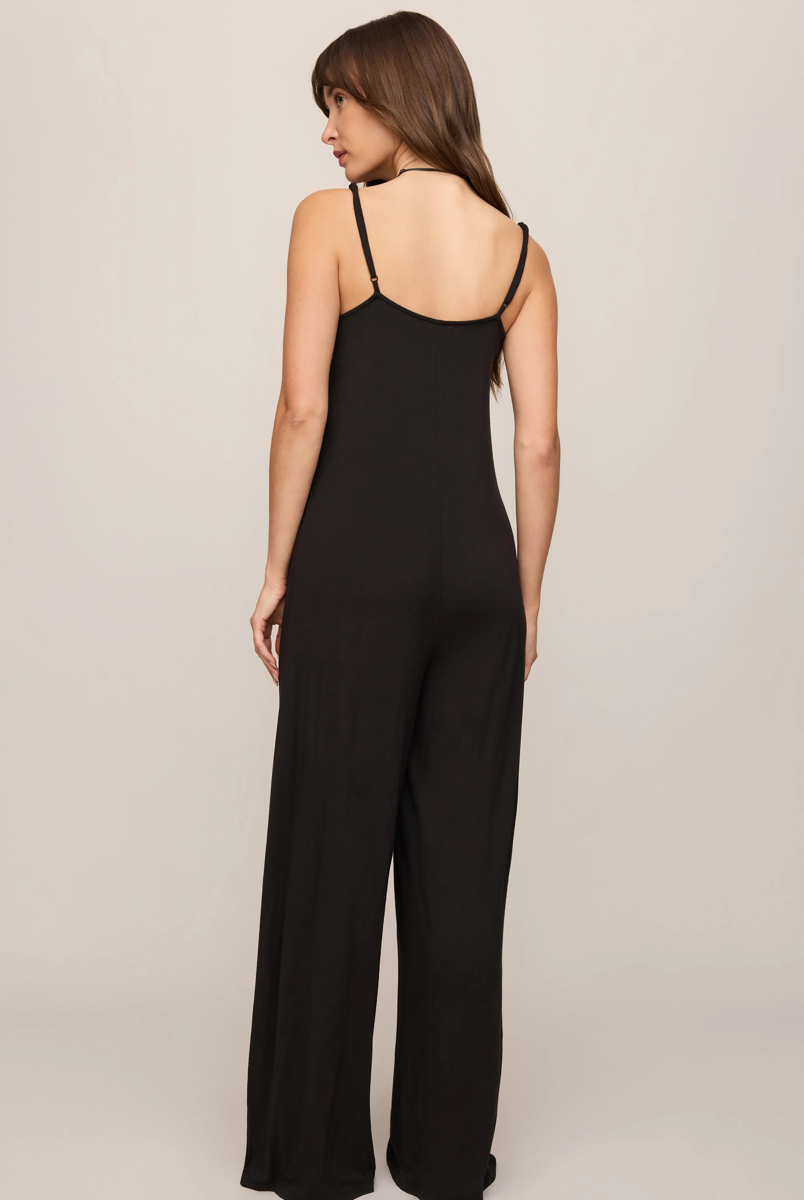 Model wearing the Z Supply Leyla Jumpsuit in black. The sleeveless jumpsuit features thin adjustable spaghetti straps, a V-neckline, a relaxed bodice with subtle seam detailing, and wide-leg pants that drape to the floor.