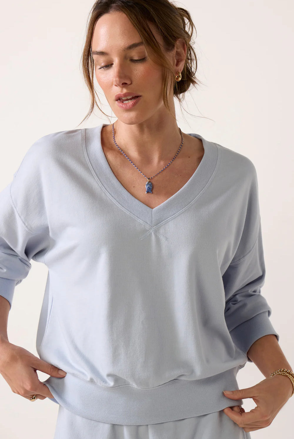 Model wearing a sky-blue V-neck sweatshirt with long sleeves, ribbed cuffs and hem, and a relaxed fit.