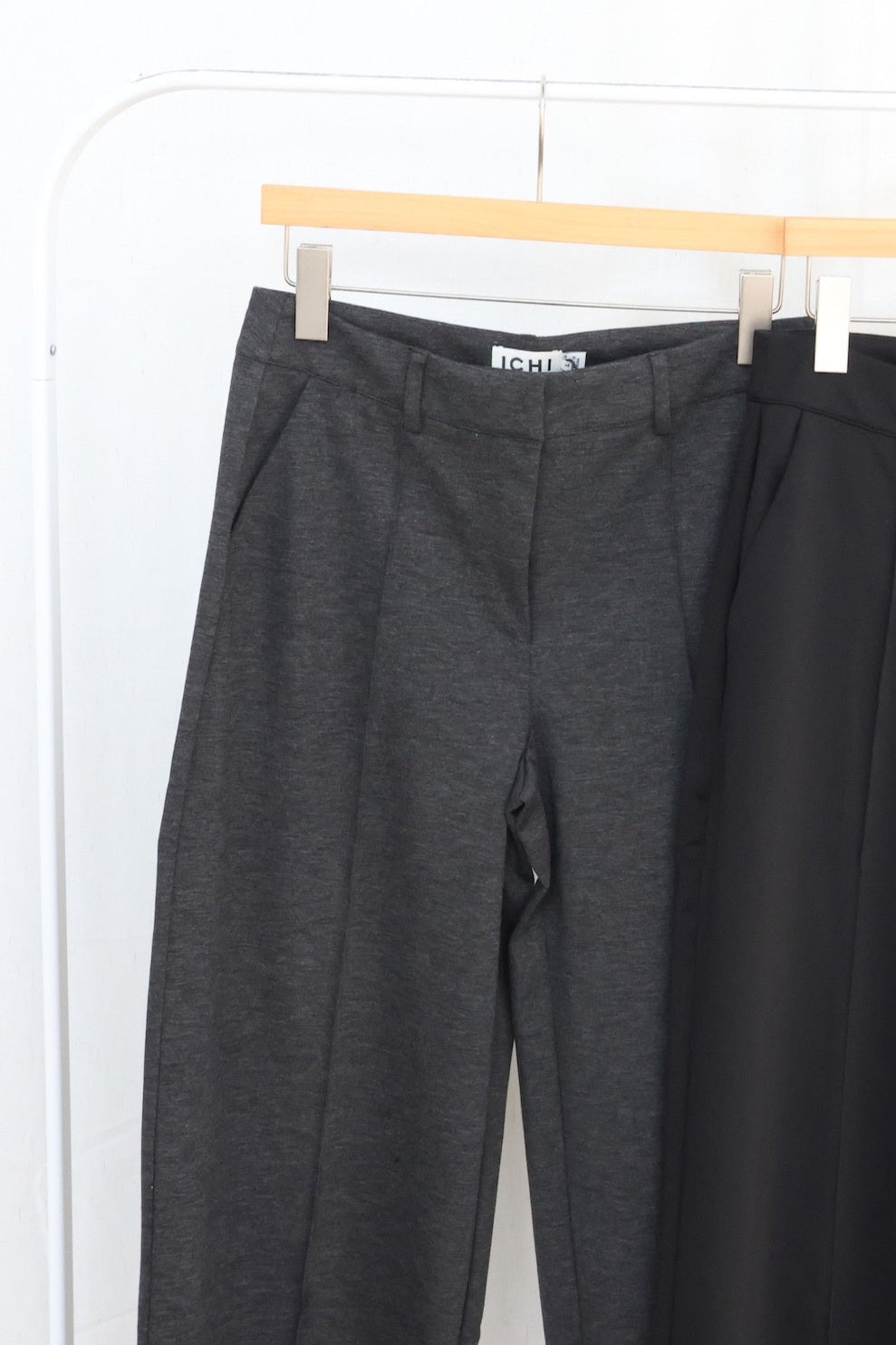 Two pairs of black pants hanging on a rack against a white background