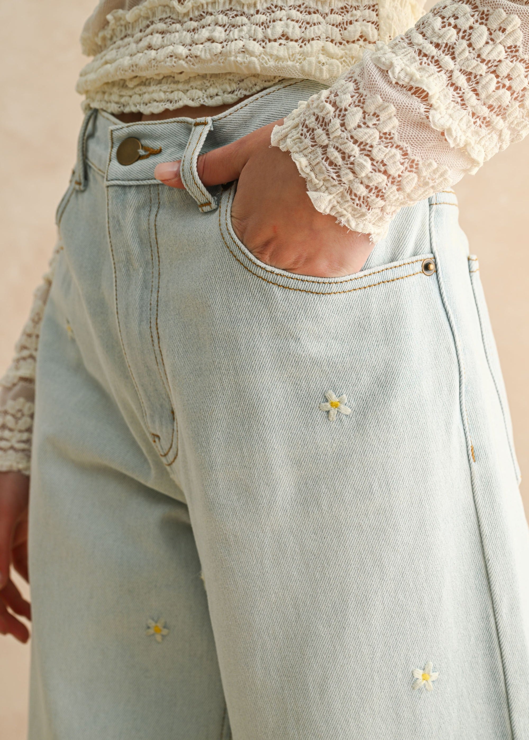 Light blue jeans with floral embroidery worn by a person, against a neutral background
