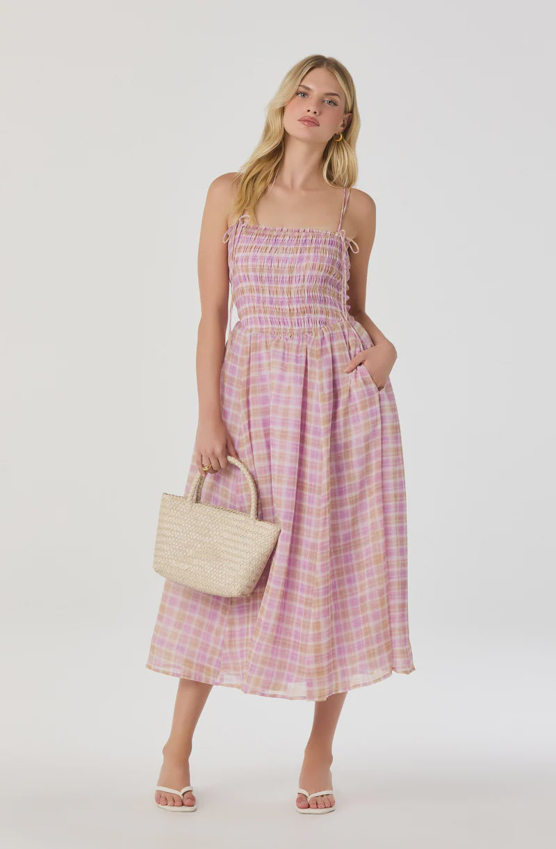 Woman wearing a pink plaid dress holding a beige handbag on a white background