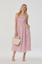 Woman wearing a pink plaid dress holding a beige handbag on a white background