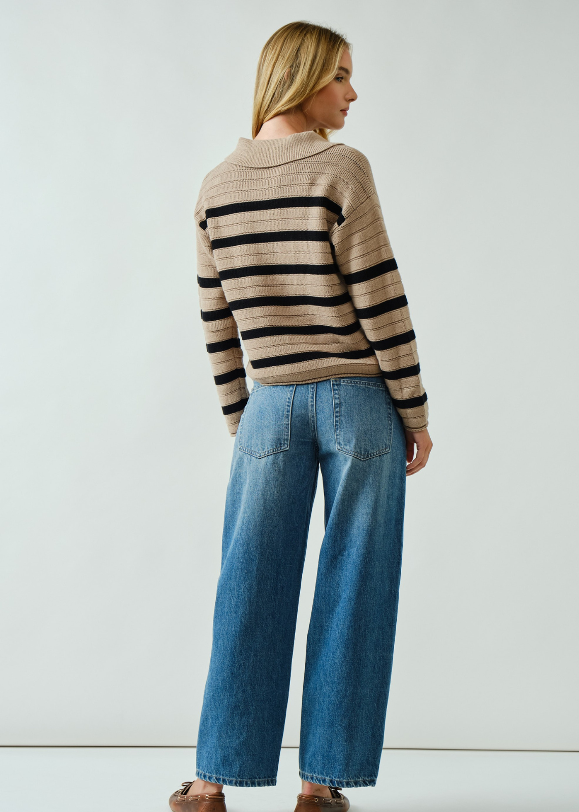 Woman wearing a striped sweater and blue jeans against a white background