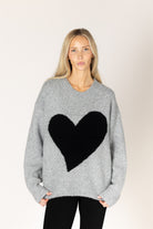 Dark grey oversized crewneck sweater featuring a bold black heart graphic on the front, with ribbed cuffs and hem.
