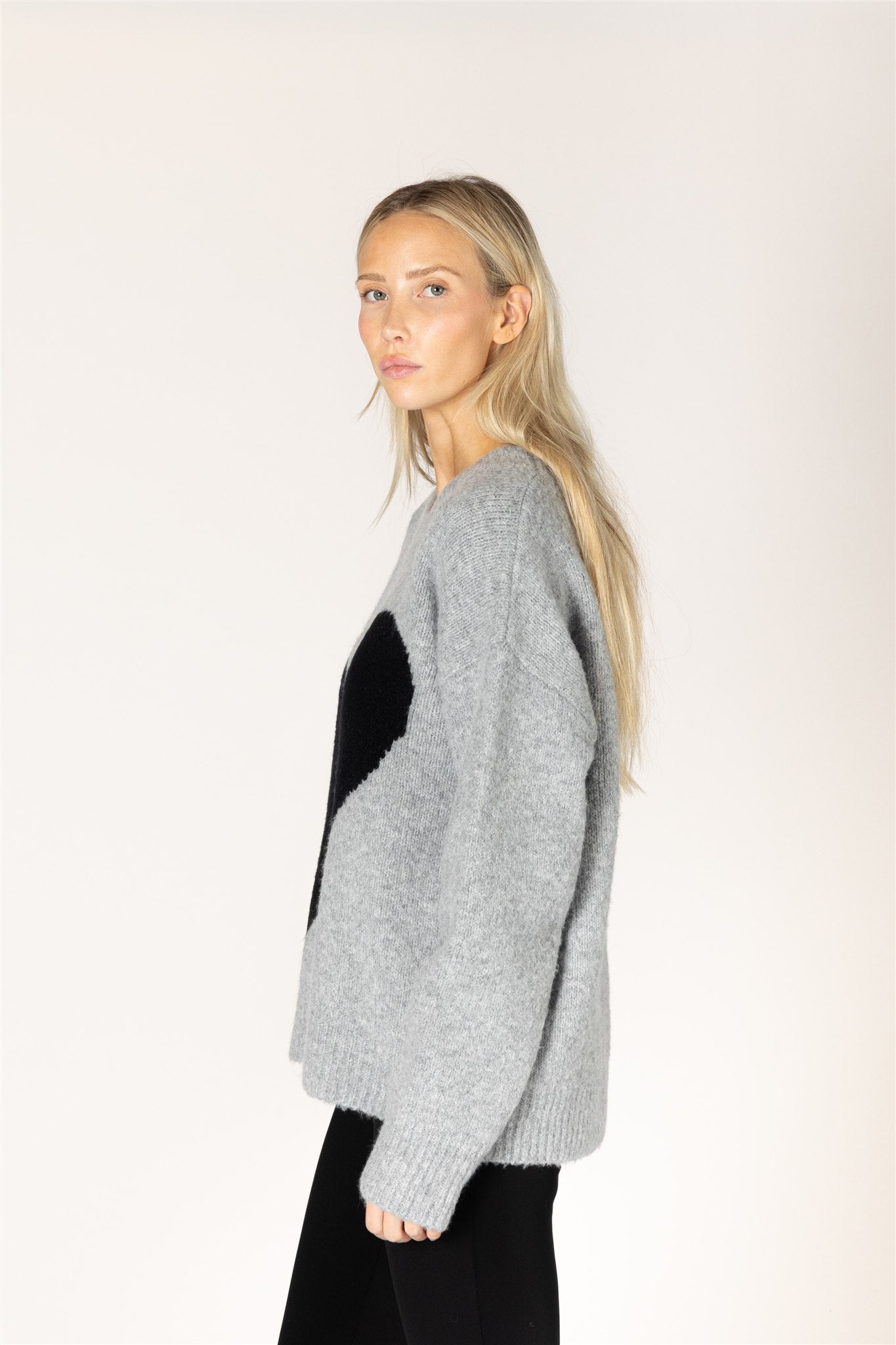 Dark grey oversized crewneck sweater featuring a bold black heart graphic on the front, with ribbed cuffs and hem.
