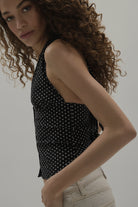 Woman wearing a black sleeveless top with white polka dots against a plain background