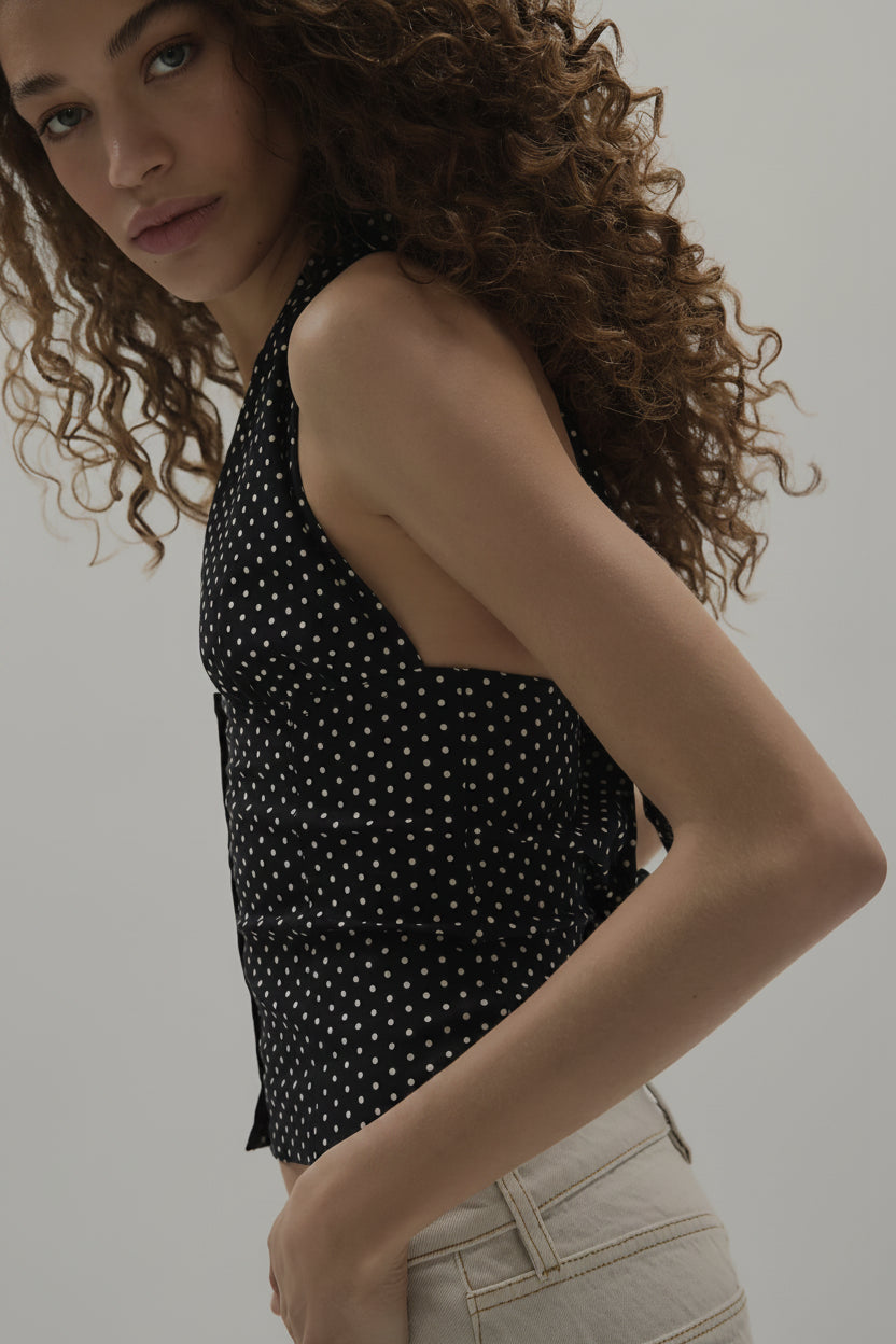 Woman wearing a black sleeveless top with white polka dots against a plain background