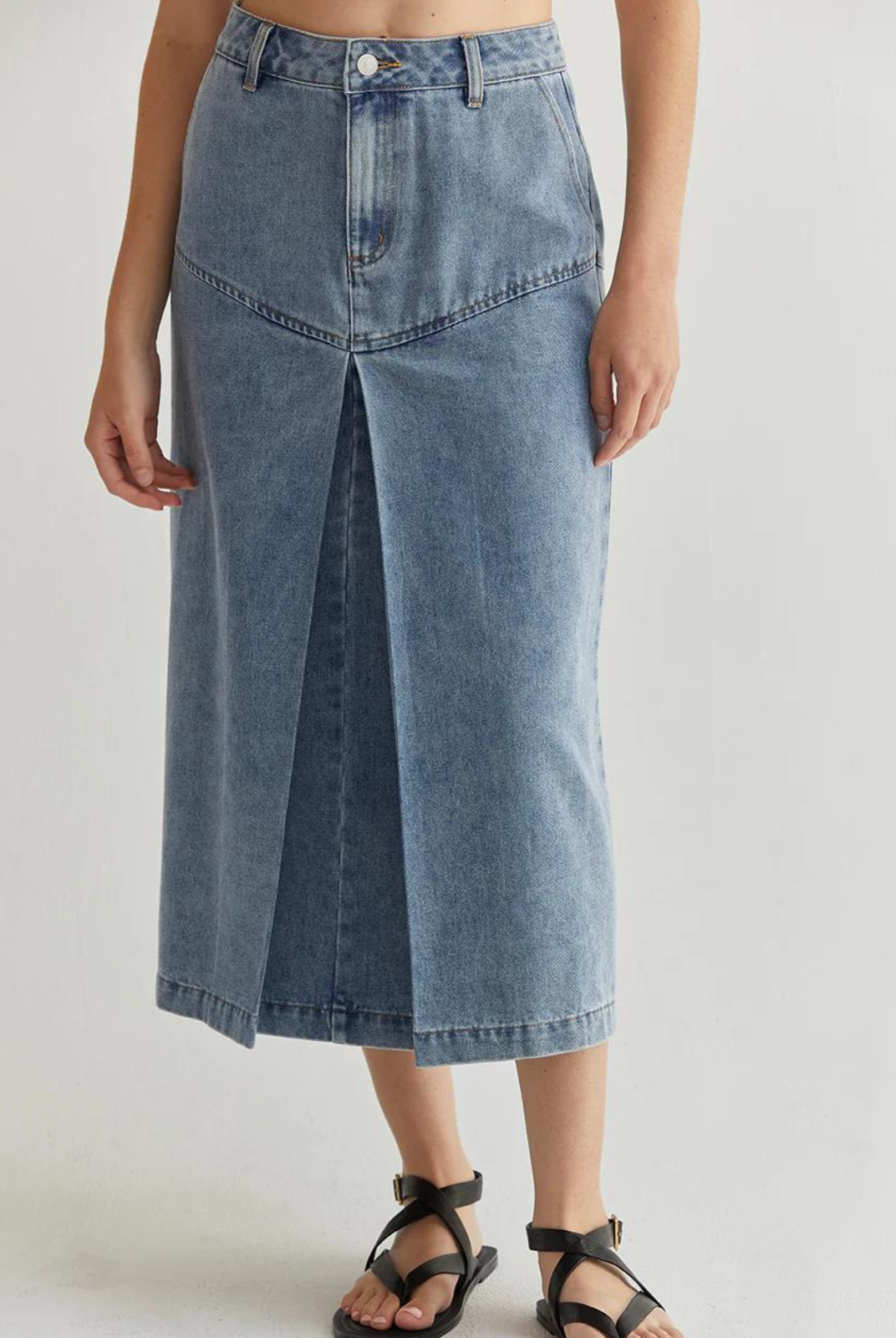 Brielle Denim Midi Skirt.The Brielle Denim Midi Skirt features a front button and zipper closure, side pockets, rear patch pocket, and angled seam on front hips that meets the inverted pleat detail.