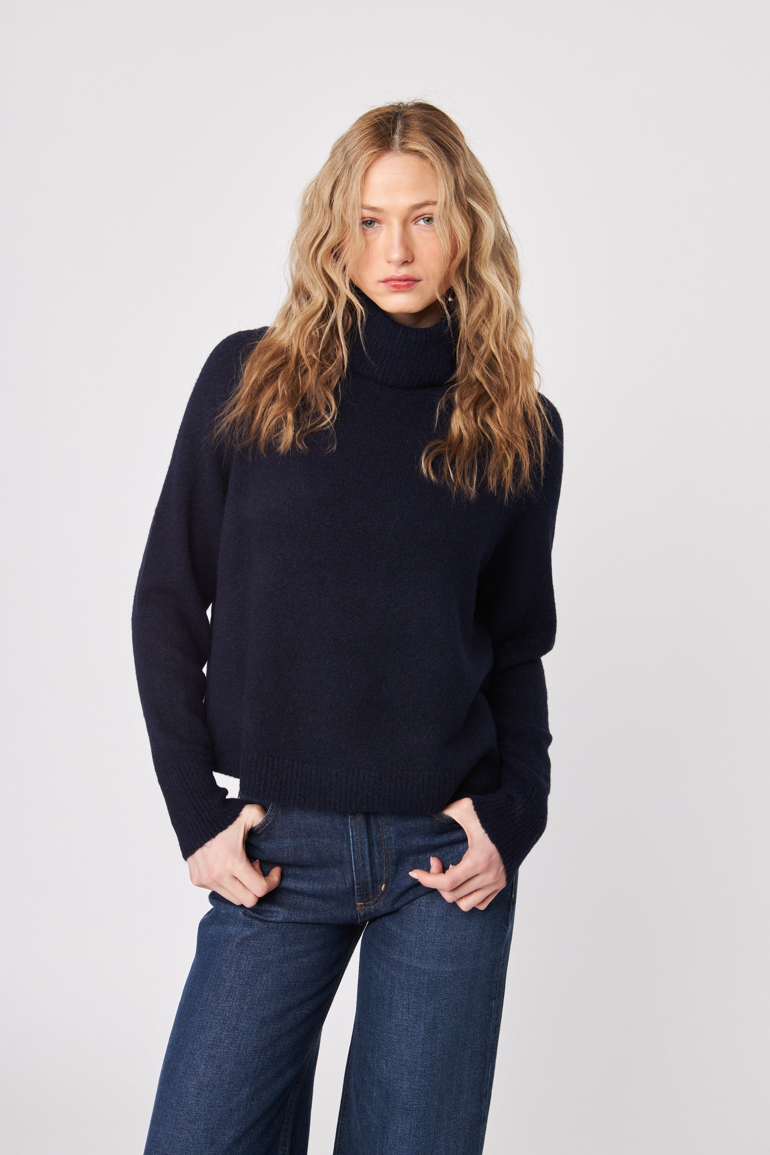 Woman wearing a black turtleneck sweater and blue jeans on a white background