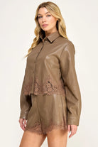 Clara Lace Trim Button-Down Top featuring a smooth faux leather finish, classic collar, long sleeves with buttoned cuffs, and delicate lace trim along the hem. Designed with a slightly cropped silhouette and a flattering, feminine fit. Pairs perfectly with the matching Clara Lace Trim Shorts for a chic, coordinated look.