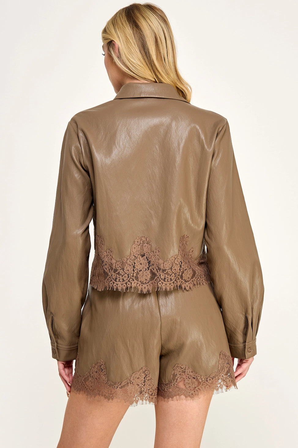 Clara Lace Trim Button-Down Top featuring a smooth faux leather finish, classic collar, long sleeves with buttoned cuffs, and delicate lace trim along the hem. Designed with a slightly cropped silhouette and a flattering, feminine fit. Pairs perfectly with the matching Clara Lace Trim Shorts for a chic, coordinated look.