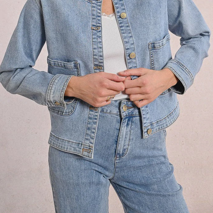 Person wearing a light blue denim jacket and jeans on a plain background