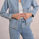 Person wearing a light blue denim jacket and jeans on a plain background