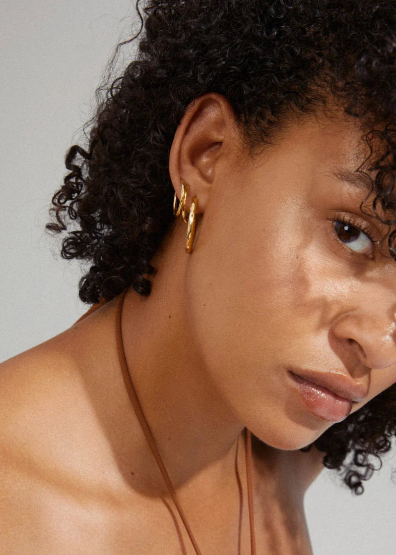 Close-up of a person with curly hair wearing gold hoop earrings against a neutral background