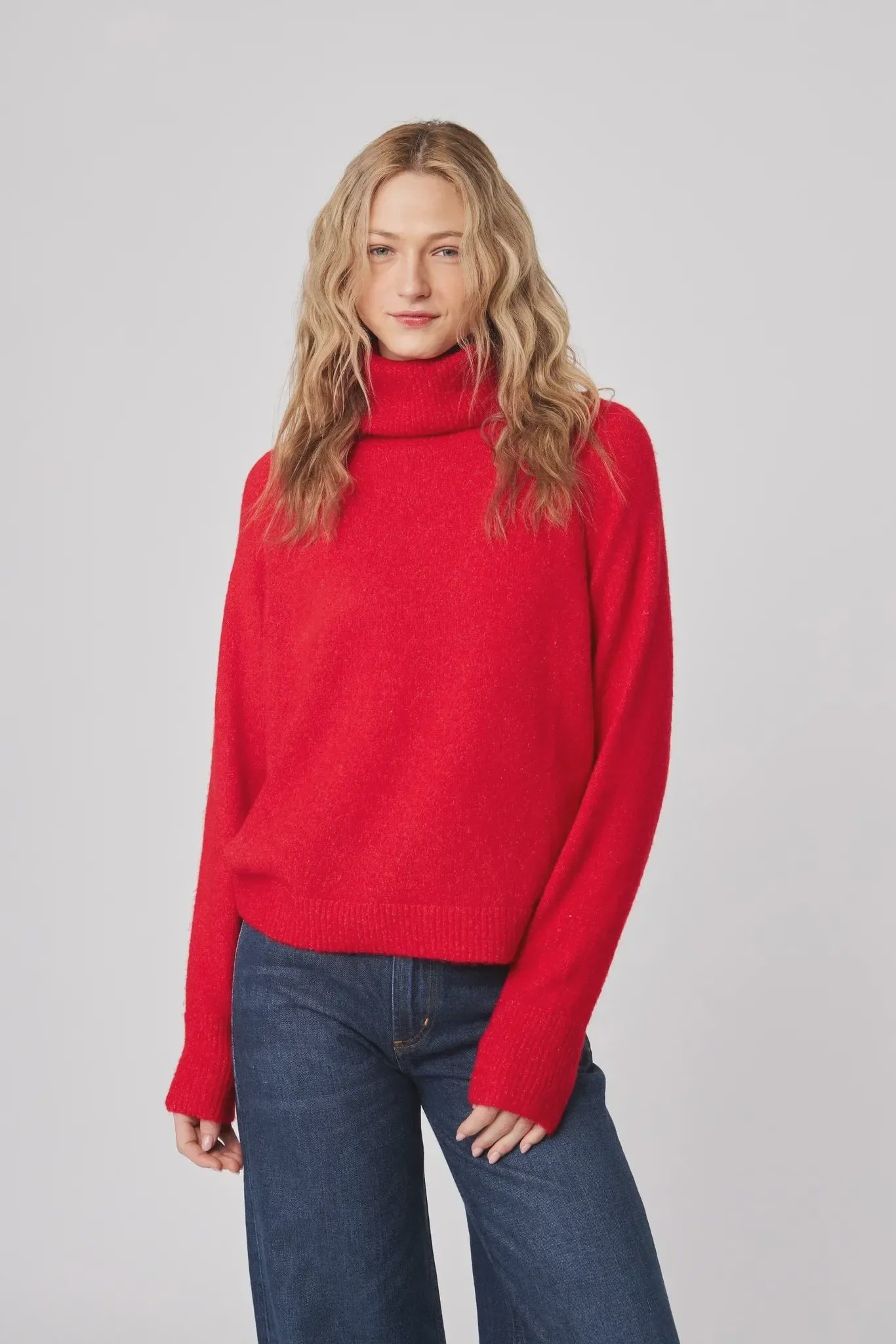 Woman wearing a red sweater and blue jeans on a gray background