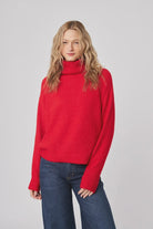 Woman wearing a red sweater and blue jeans on a gray background