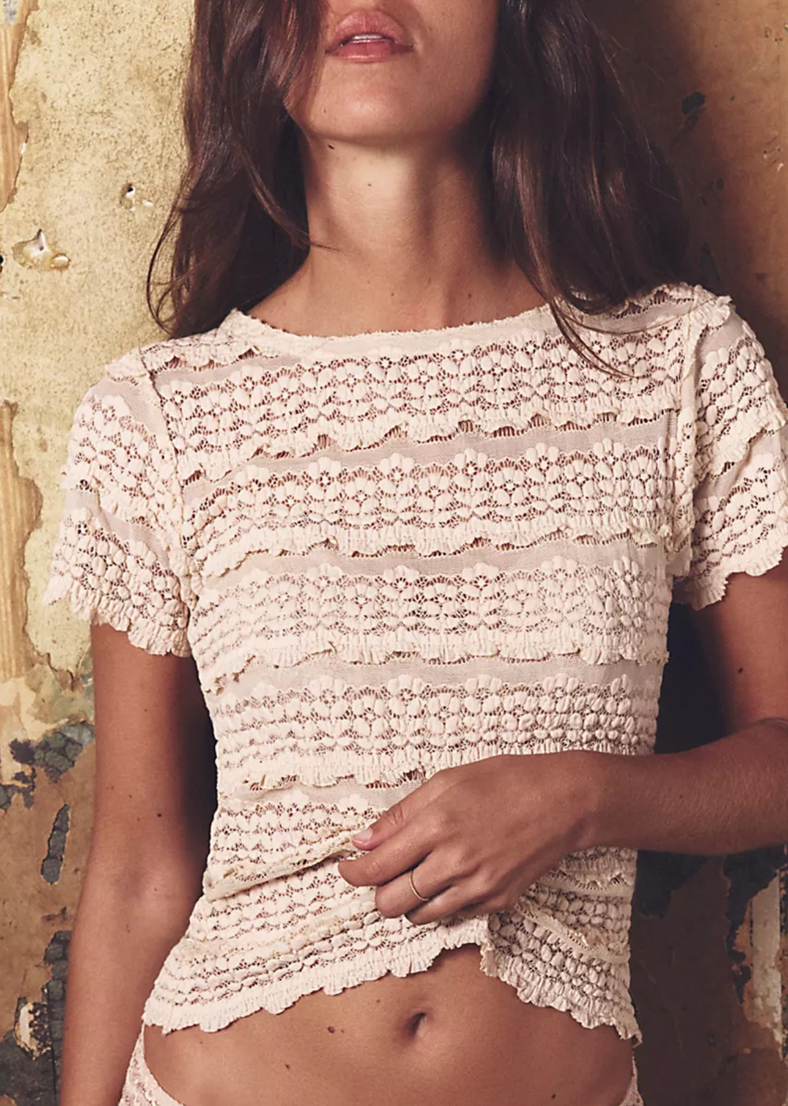 Woman wearing a lace top against a textured wall.