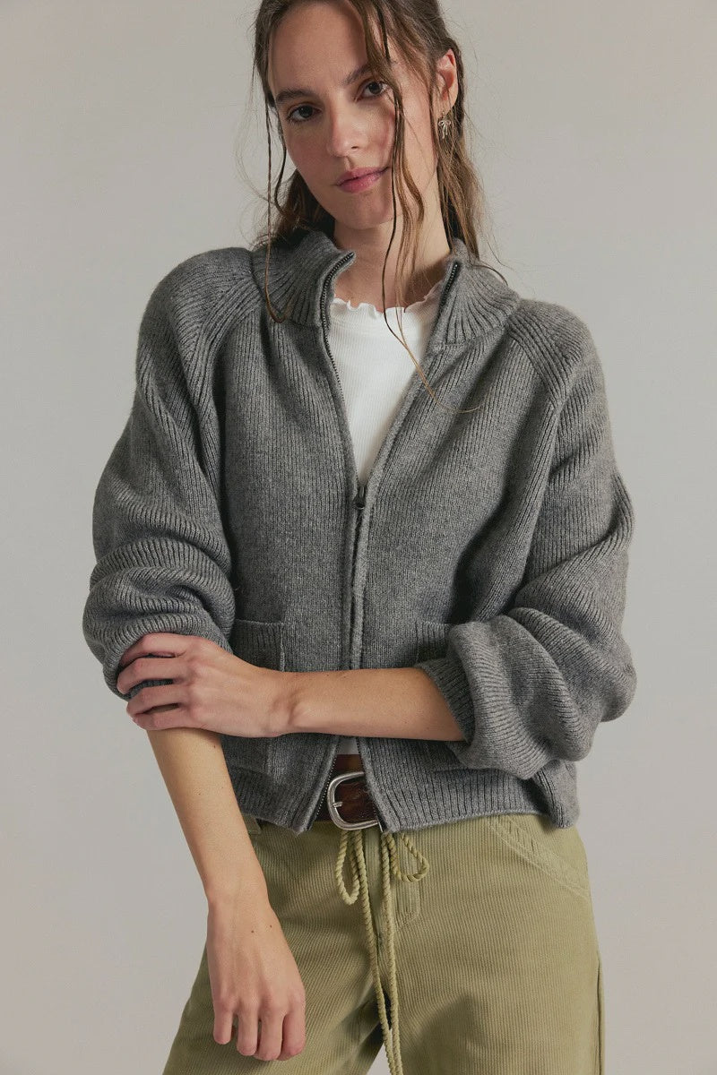 Women's ribbed knit zip-front sweater in cool grey with a high turtleneck collar, raglan sleeves, and front patch pockets.